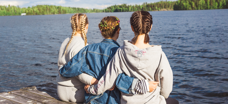Tre piger sidder på en badebro med ryggen til.