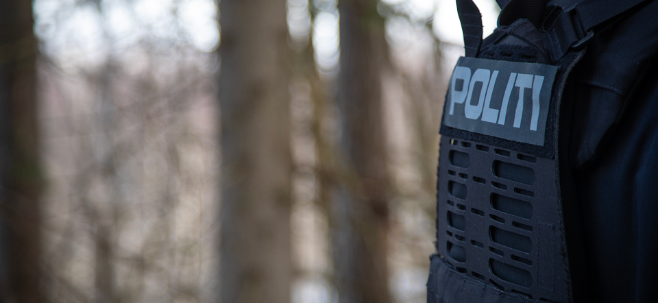 The back of a police officer. Trees in the background.